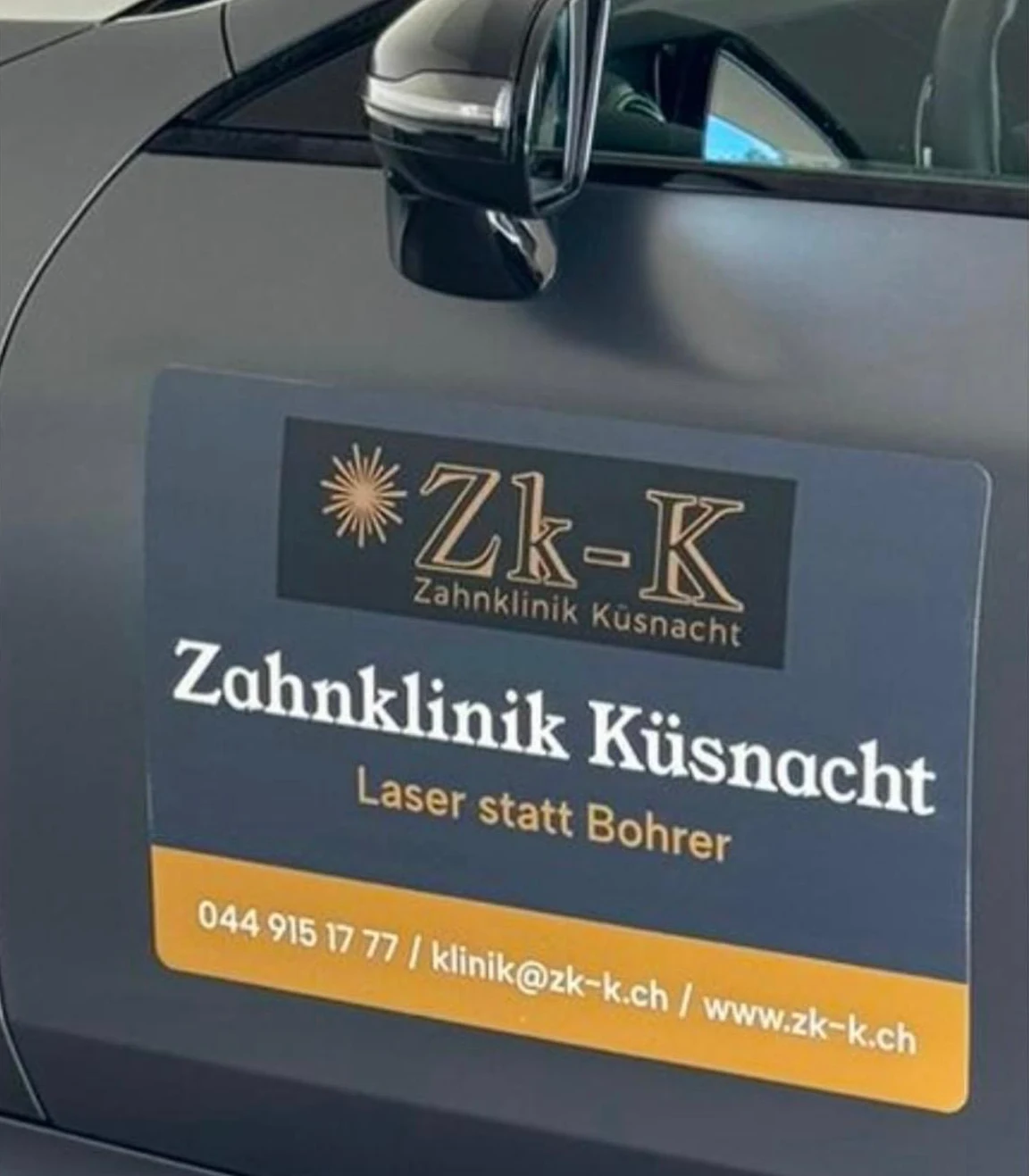Autotür mit dem Schild der Zahnklinik Küsnacht: Zk-K-Logo, «Laser statt Bohrer», Telefon 044 915 17 77, klinik@zk-k.ch und www.zk-k.ch